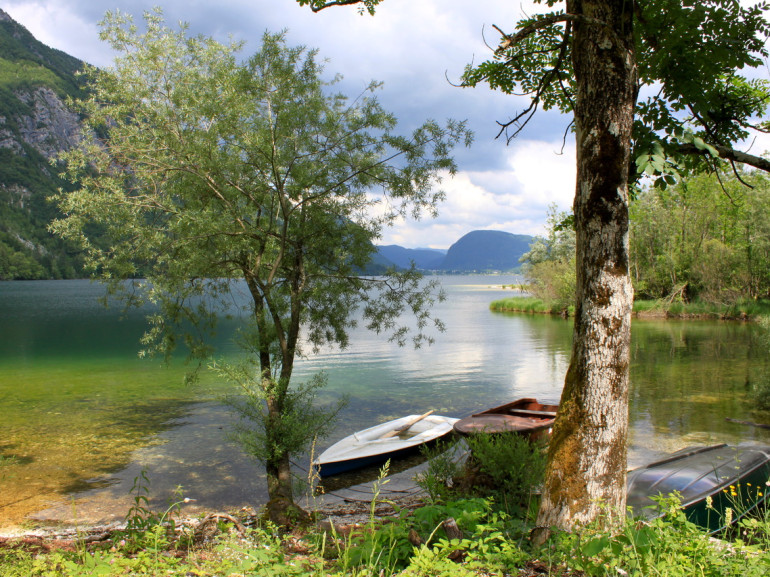 il lago visto dalla riva, circondato da montagne. due barche in legno vicino alla spiaggia